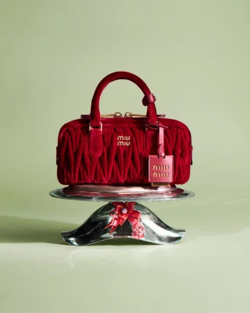 Red velvet handbag with gold hardware displayed on a silver decorative stand against a pale green background
