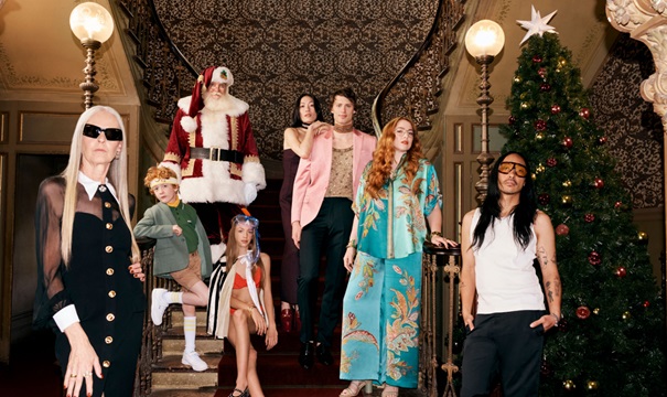 A diverse group of people pose on a staircase next to a Christmas tree, with one person dressed as Santa Claus. 
