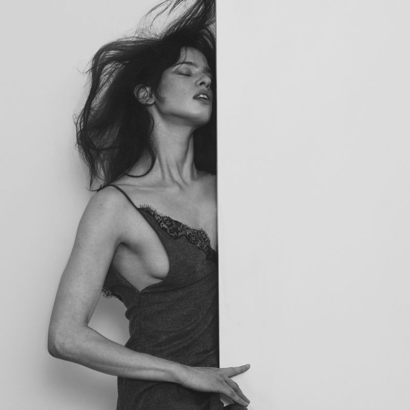 Black and white portrait of a woman with dark hair blowing, wearing a slip dress, standing next to a blank white space.