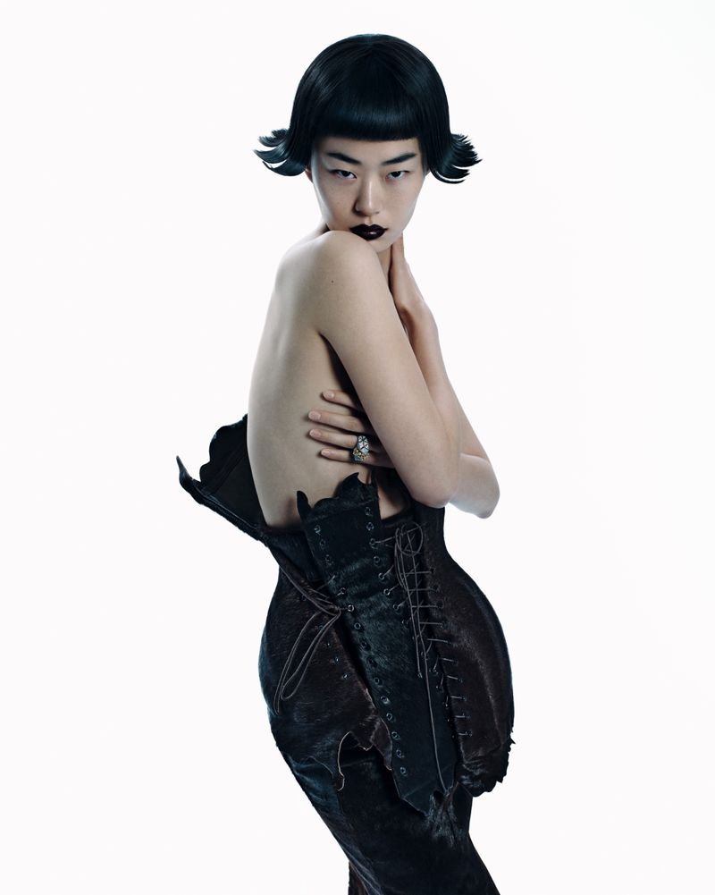 Elegant studio shot of an Asian woman with dark lipstick and hair, wearing a lace-up black garment against a clean white backdrop.