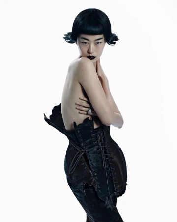 Elegant studio shot of an Asian woman with dark lipstick and hair, wearing a lace-up black garment against a clean white backdrop.