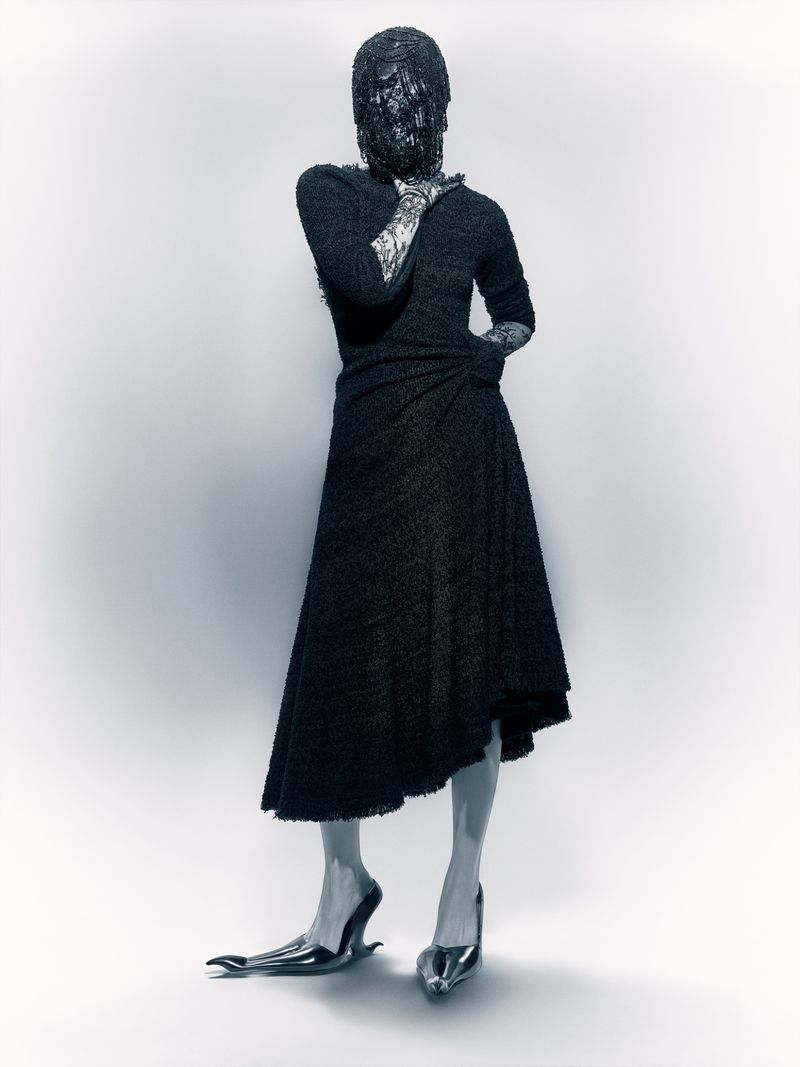 Abstract fashion image showcasing a person in a textured black dress with an obscured face and avant-garde footwear against a light background.