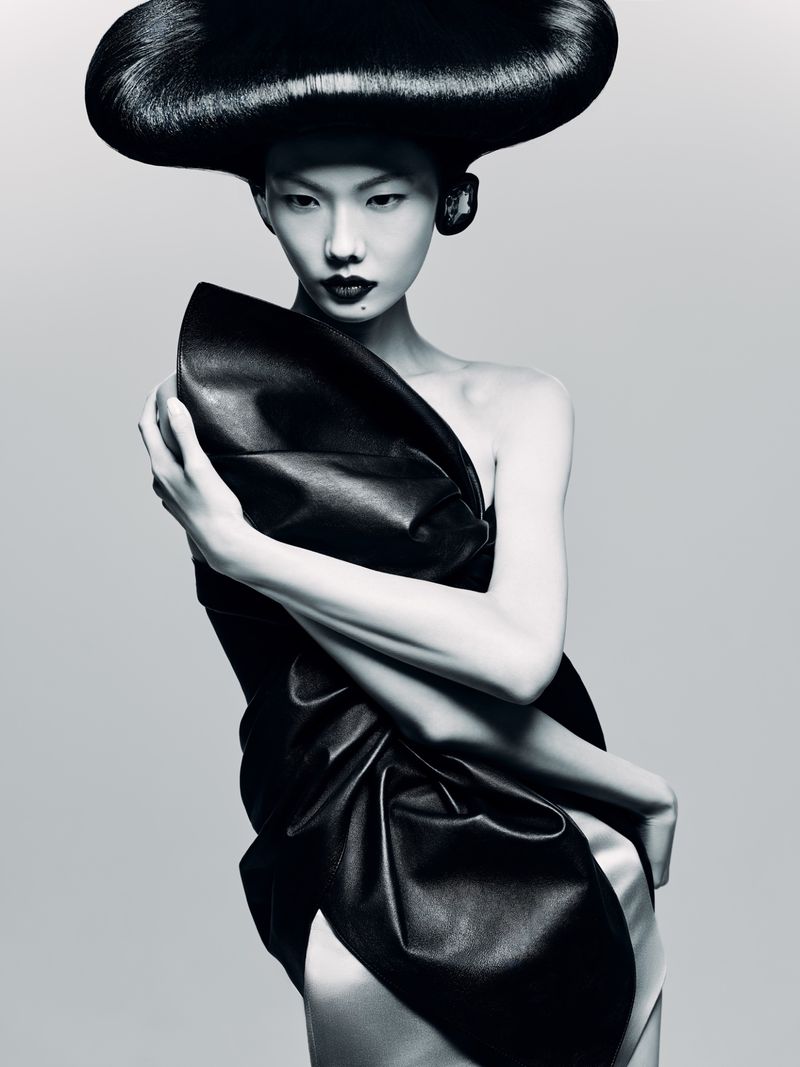 Woman with dramatic dark hair and a draped black dress poses in a studio. Beauty and fashion photography with an Asian model.