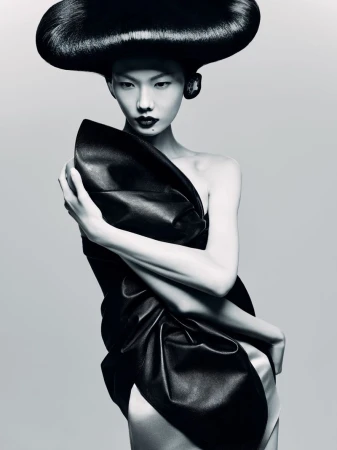 Woman with dramatic dark hair and a draped black dress poses in a studio. Beauty and fashion photography with an Asian model.