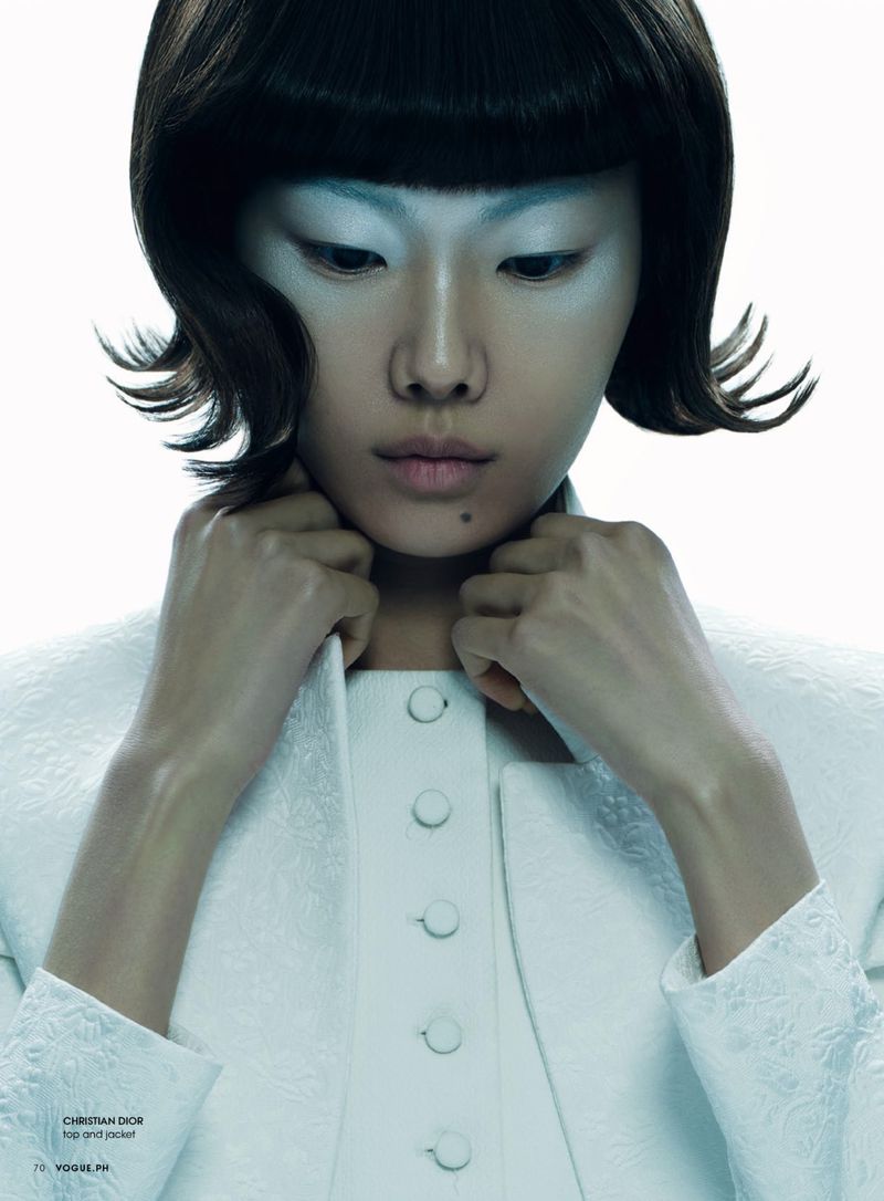 Elegant, ethereal portrait of an Asian woman with short dark hair and alabaster skin, wearing a white dress and jacket in a bright studio.