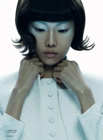 Elegant, ethereal portrait of an Asian woman with short dark hair and alabaster skin, wearing a white dress and jacket in a bright studio.