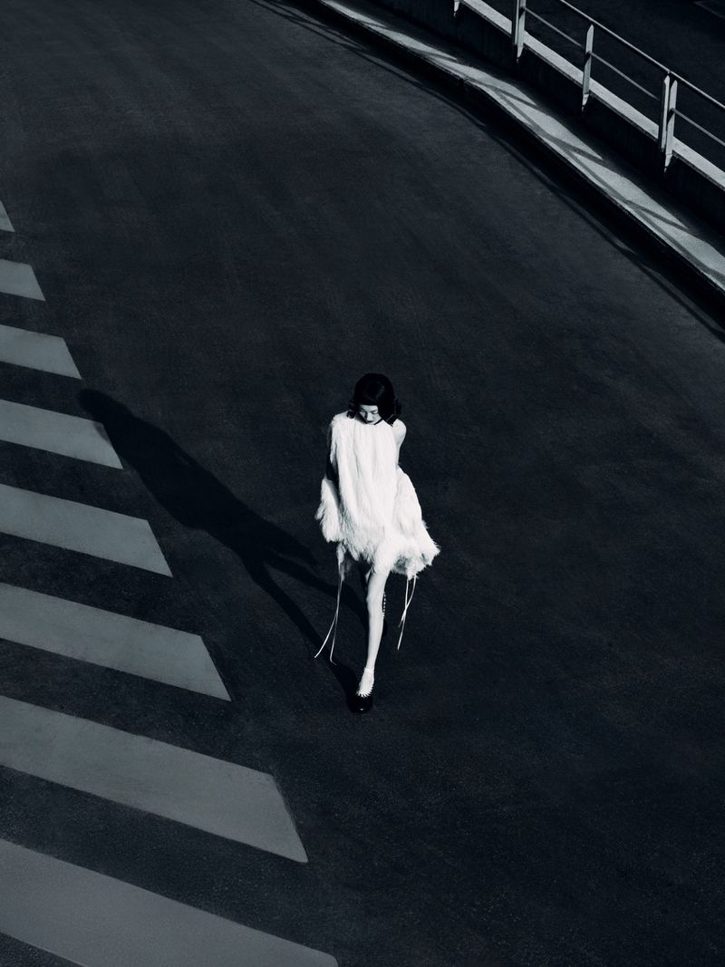 Fashion shot of a woman in a white dress walking on a crosswalk. The image is captured from a high angle in black and white.