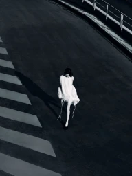 High-angle fashion photograph of a model in a white dress walking down an asphalt ramp with striped road markings.