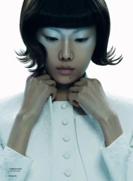 Model with bob haircut and pale makeup adjusting white buttoned jacket against white background