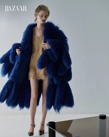 Model wearing a blue faux fur coat over a beige lace dress against a plain studio background