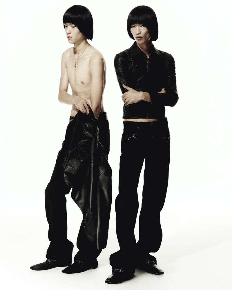 Two Asian male models posing in black leather jackets and black pants against a white background in a fashion studio shoot.
