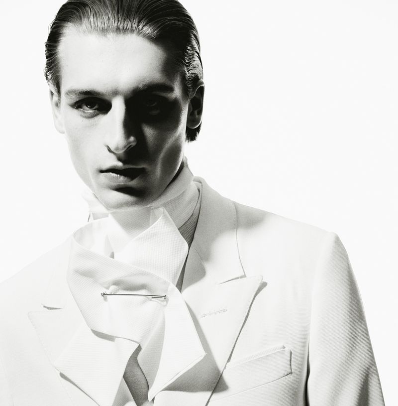 Studio portrait of a young adult man wearing a white suit and ascot, looking directly at the camera with bright illumination.
