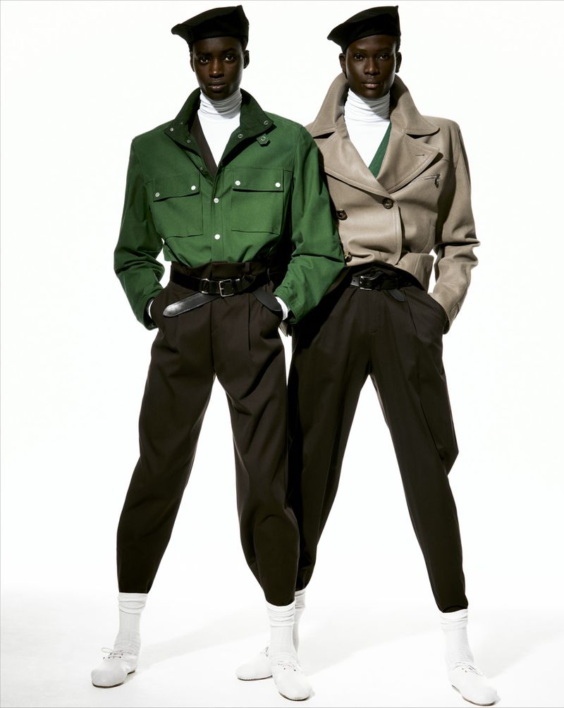 Two dark-skinned men in green and beige jackets, black pants, berets, and white socks pose in a bright studio fashion shot.