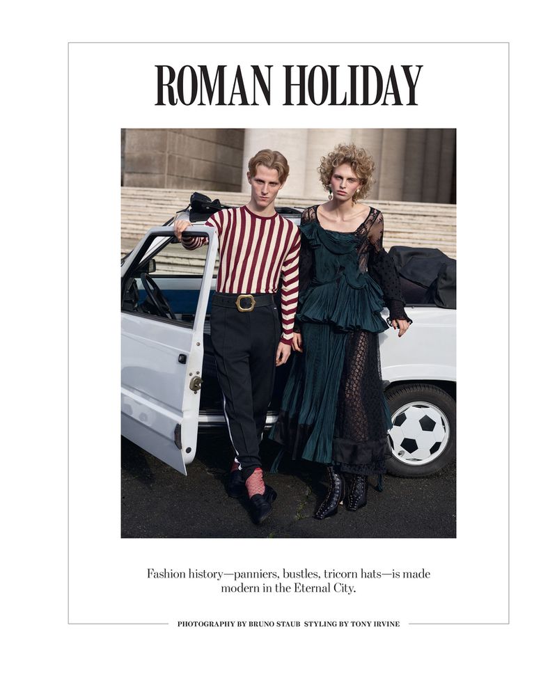 Editorial fashion shot of a male and female model in designer clothing posed by a white car against a classical building backdrop.