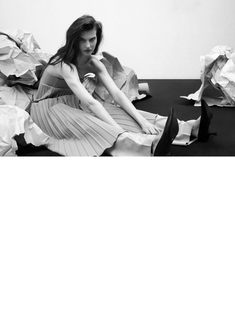 Monochrome fashion shot of a woman with long hair wearing a dress, surrounded by crumpled paper on a black and white background.
