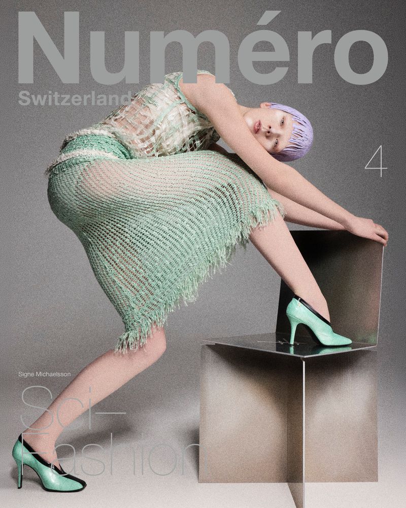 Editorial fashion shot: Woman with lavender hair in knitted dress poses on metallic cube seat against a gray background, wearing matching high heels.