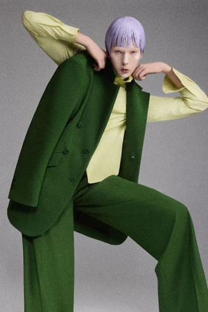 Model with purple hair wearing a green suit and yellow shirt against a grey studio backdrop for Numero Switzerland