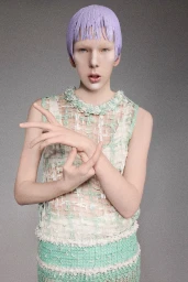 Model with purple hair wearing a textured mint green sleeveless top against a grey seamless background.