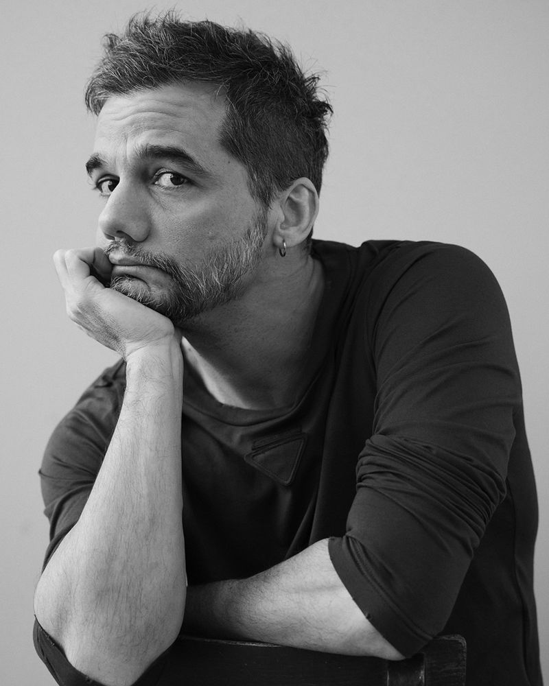 Black and white portrait of a middle-aged man with a beard, resting his chin on his hand in a thoughtful pose against a plain backdrop.