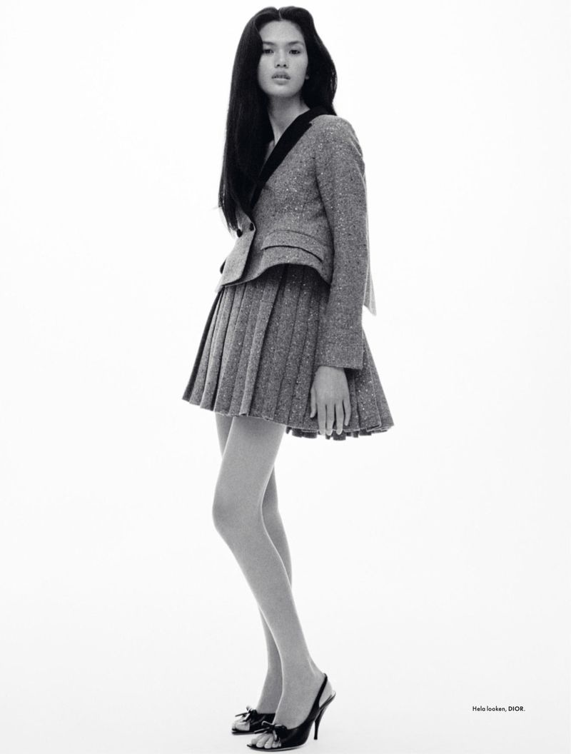 Full-length portrait of a young Asian woman wearing a gray tweed skirt suit and black heels, posing in front of a white backdrop.