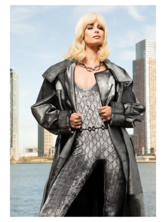 Model Taylor Hill wearing a metallic coat and patterned jumpsuit with a city skyline and water background