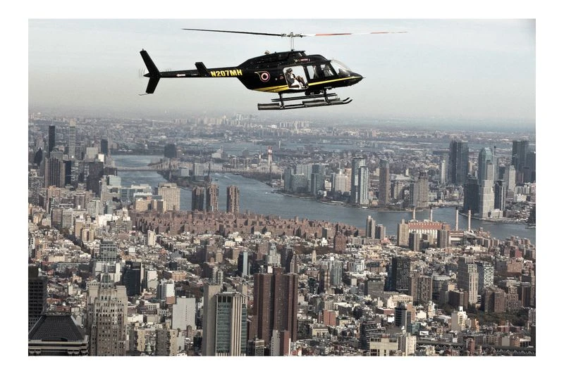 Helicopter flies over a densely populated urban cityscape with numerous tall buildings and waterways on a hazy day.