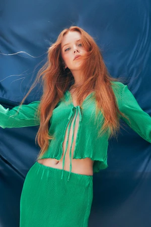 Abigail Cowen with long red hair wearing a green top and skirt against a draped blue fabric background for Numero Netherlands.