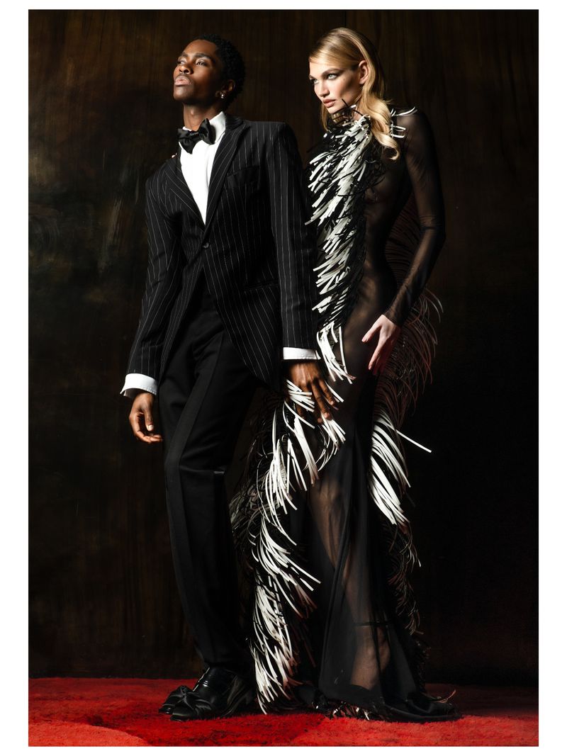 A stylish interracial couple posing in formal attire against a dark backdrop, showcasing fashion and elegance with a touch of glamour.