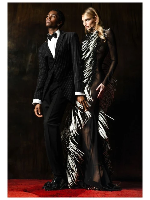 A stylish interracial couple posing in formal attire against a dark backdrop, showcasing fashion and elegance with a touch of glamour.
