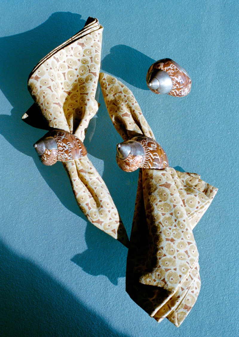 Elevated shot of beige patterned napkins adorned with decorative napkin rings featuring silver accents against a blue surface.
