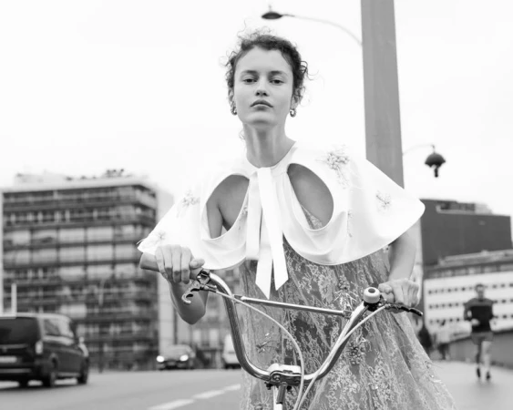 Model in a white cutout cape and lace dress riding a bicycle outdoors in Paris for L'Officiel Italia.