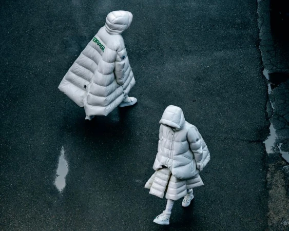 Overhead shot of two people wearing puffy white coats and sneakers walking on a textured grey surface with the word BRASIL on a coat.