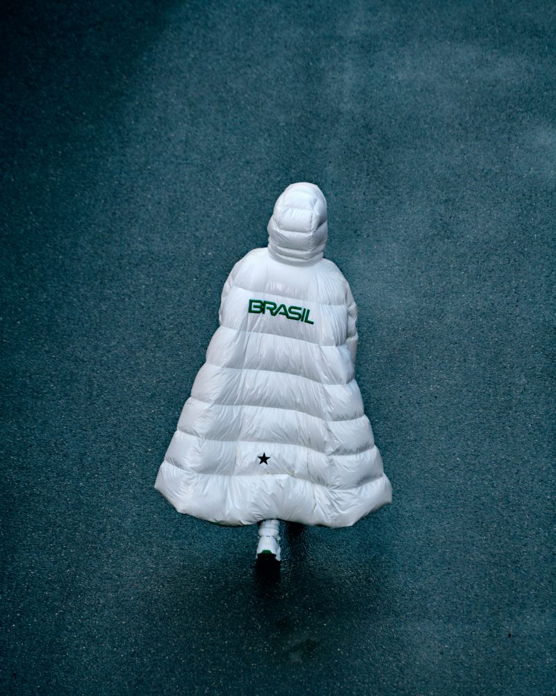 Aerial view of a person in a white hooded puffer coat that reads 'Brasil' in green against a speckled blue-gray background.