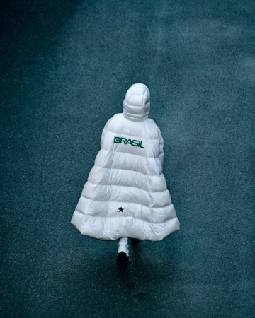 Aerial view of a person in a white hooded puffer coat that reads 'Brasil' in green against a speckled blue-gray background.