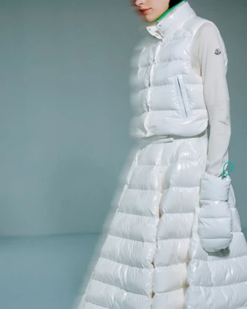 Woman in puffy white Moncler vest and skirt with matching hand warmer in a studio setting on a light gray background.