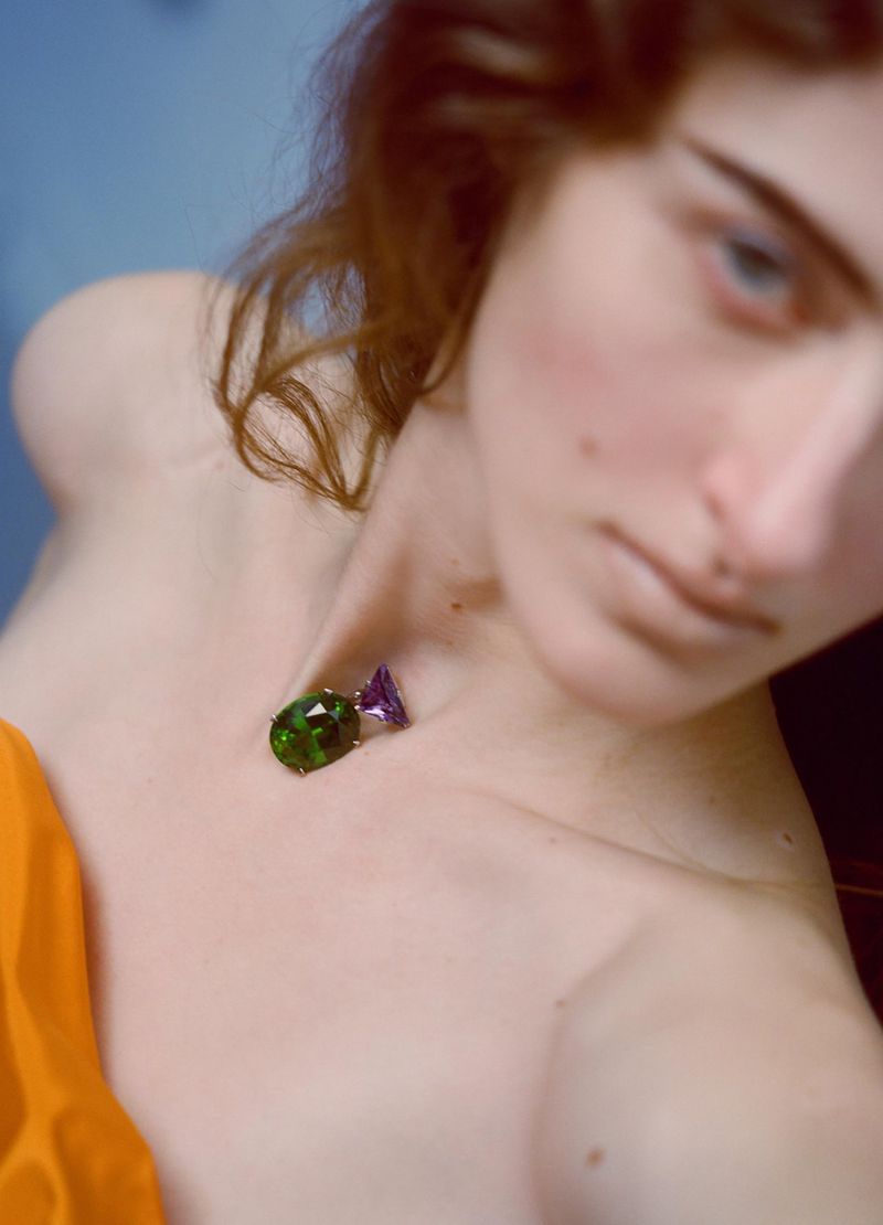 Close-up of a fair-skinned woman with loose auburn hair wearing a gemstone necklace, gazing off-camera with a shallow depth of field.
