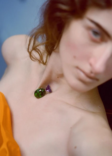 Close-up of a fair-skinned woman with loose auburn hair wearing a gemstone necklace, gazing off-camera with a shallow depth of field.