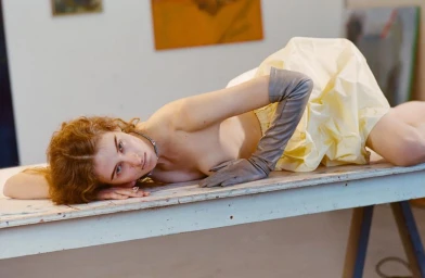 Model lying on a white table wearing a yellow skirt and grey gloves for an editorial shoot by Brianna Capozzi.
