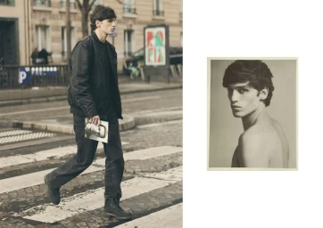 Man in black bomber jacket and dark jeans walking across a city street, holding a small framed portrait.