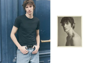 Young man wearing a black t-shirt and light blue jeans standing against a dark blue paneled door with an inset black and white portrait.