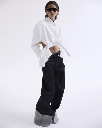 A woman poses in an open white shirt and wide-leg dark jeans against a white background, showcasing a casual yet fashionable look.