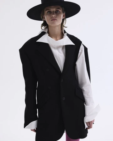 Fashion photo of a woman wearing a black blazer, wide-brimmed hat, and white blouse against a white backdrop in a studio setting.