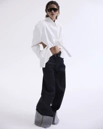 Model wearing oversized white cut-out shirt and dark denim jeans against a white seamless background