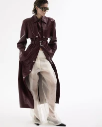 Model in burgundy leather coat and sheer trousers against a bright white background for Amica Volume 80
