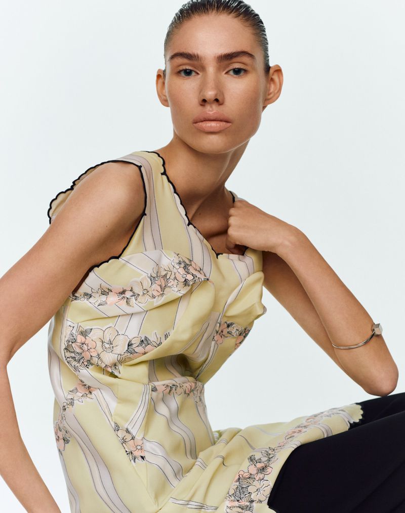 Model Cara Schadel wearing a yellow floral sleeveless dress against a plain white studio background.
