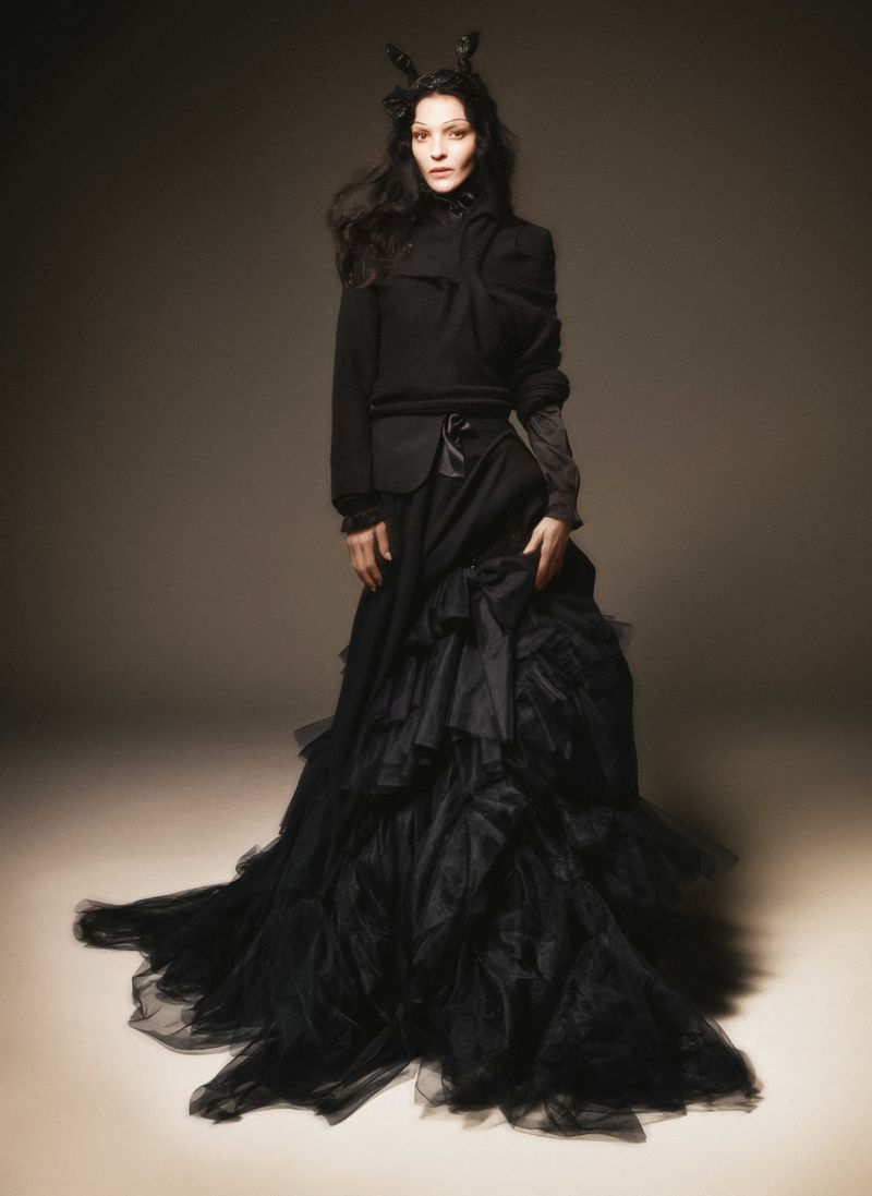 Fashionable woman in black dress with ornate tulle skirt, posing indoors against soft background. Fashion editorial with artistic lighting.