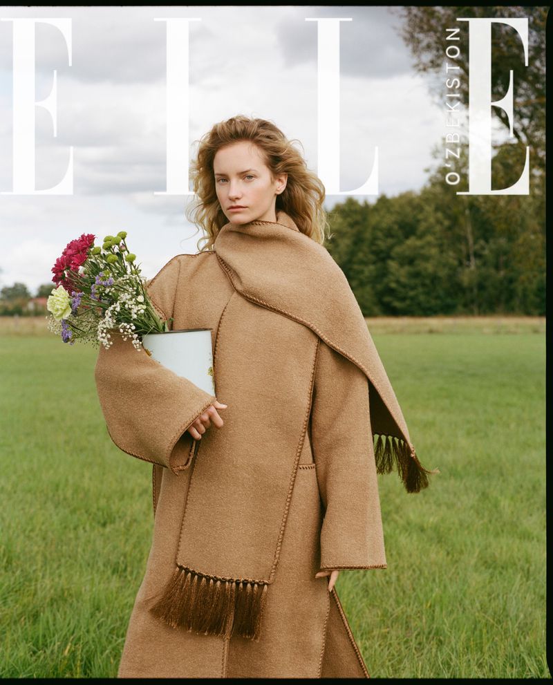 Elle magazine cover featuring a woman in a tan coat holding flowers, standing in a green field under a cloudy sky.