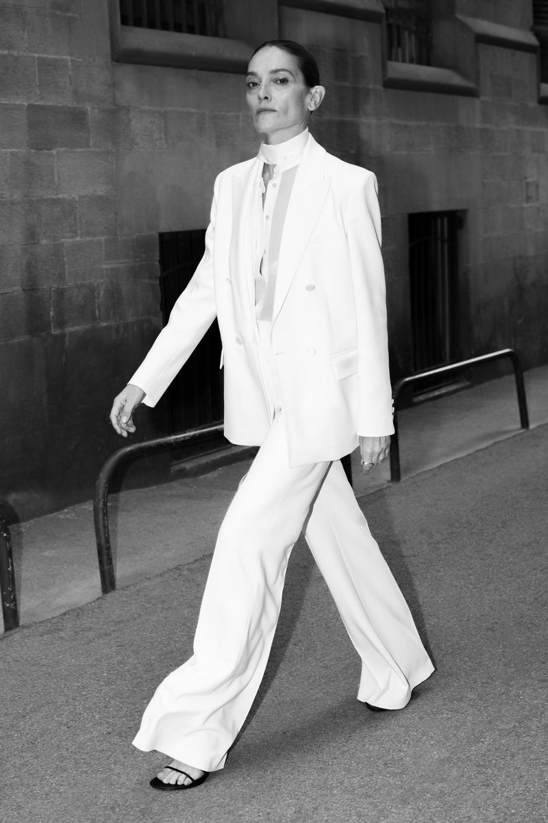 Elegant woman strides confidently in a white suit on an urban street, creating a high-fashion black and white editorial image.