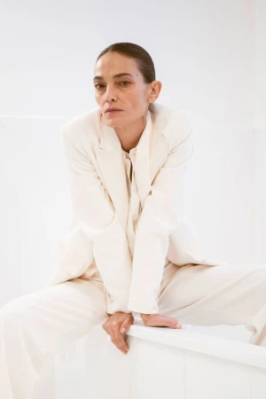 Model Laura Ponte in an ivory suit leaning forward against a plain white studio background for Mango