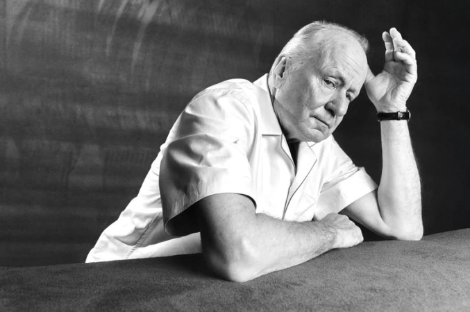 Black and white portrait of an older man with white hair wearing a short-sleeved collared shirt resting his head on his hand.